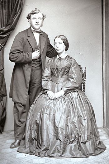 Lærer Søren Jensen ved den Brock-Bredalske Skole i Randers og hans hustru Stine Jensen fotograferet i midten af 1860’erne. Søren Jensen er iført sort jakke, bukser og vest, mens Stine Jensen er iklædt en krionlinekjole af silke.