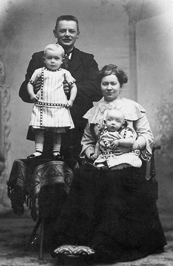 Kobbersmed og blikkenslager Magnus Anthony med hustruen Mariane Anthony og deres to børn, Carl og Gudrun. Familien er fotograferet omkring 1907 i Randers. Begge børn uanset køn er iført kjoler.